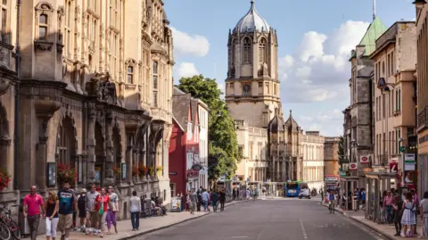 Getty Images A street view of the city of Oxford with people walking along the pavements and Christ Church cathedral can be seen rising above the rooftops at the end of the road.