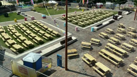 A public square with lots of wooden benches, bunting and flags