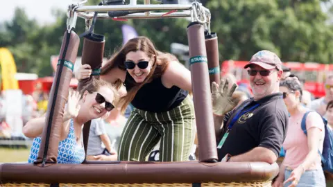 International Bristol Balloon Fiesta Two women and a balloonist pictured inside a hot air balloon basket smile and wave at the camera