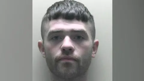 A mugshot of a man called Findlay Mackay. He has short dark hair which has been shaved round the sides but left slightly longer on top. He has a trimmed dark beard.