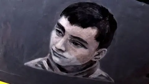 Getty Images Close up of the helmet featuring a black and white image of Dmytro Sarpar, who has dark hair and thick eyebrows.