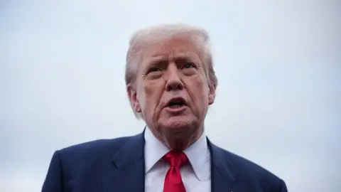 Getty Images Headshot of Donald Trump talking. He is wearing a dark suit jacket, white shirt and red tie.
