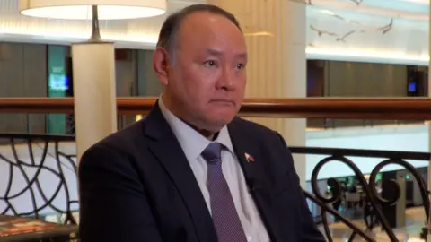 Philippines defence minister Gilberto Teodoro Jr wearing a dark suit and purple tie sitting on a balcony during an interview with the BBC.