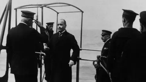 Getty Images The head of the Fascist government Benito Mussolini welcomed by the admiral while boarding battleship Cavour with a bandaid over his nose.