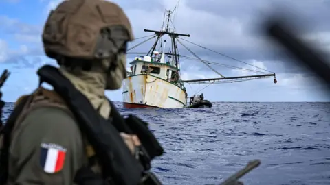 Préfecture maritime de l'Atlantique/X A man in military uniform, with a French flag insignia on his sleeve, looks out at a ship at sea.