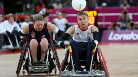 PA Media Wheelchair rugby players compete for the ball during a match at London 2012, with Steve Brown in a white Great Britain shirt and another in a dark USA kit racing side by side in specialised sports wheelchairs.
