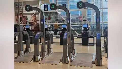 You checkout the three huge parameters in front of the Tesco scan as you checkout. They have a large metal plate on the ground and have a number of above one to three from both sides. Reddit users have posted that they look like airport security scanners.