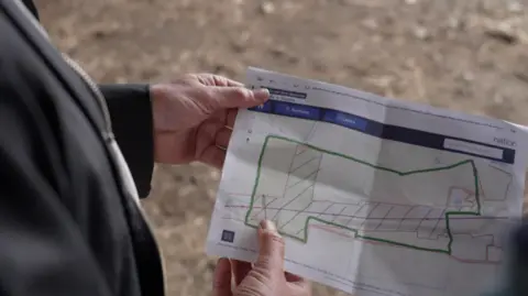 Jon Homer is holding a National Grid diagram which shows the company's proposal for his farm and the pylon route that will cross his land.