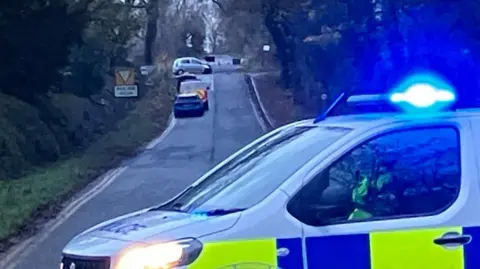BBC/Seb Cheer A photo showing a light-coloured Hyundai i10 car in the background, with a police van blocking the road up to it.