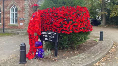 The Adlington Village Hall sign with a soldier and dog made from bright red poppies.