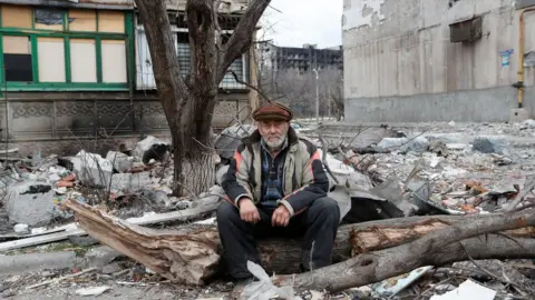 Reuters A local resident sits near a damaged apartment building in Mariupol