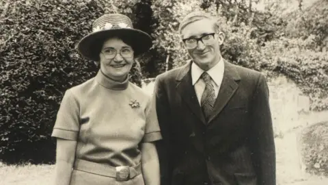Contributed A black and white photo of a man and woman standing together. They wear smart clothing and are standing outside. 