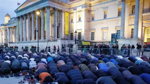 Dozens of people bowed in prayer, as the sun sets over the National Gallery building in Trafalgar Square