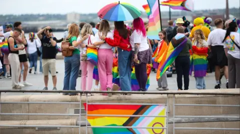 Pride parade with lots of colours, flags and people smiling.