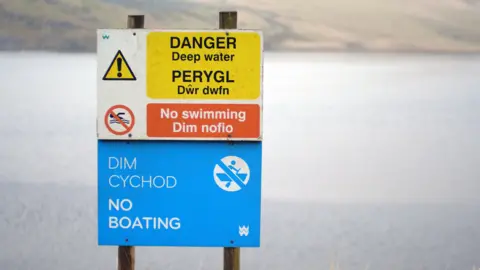 A sign at the edge of the reservoir reads "danger", "no swimming" and "no boating". The water of the reservoir is visible behind the sign.