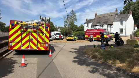 Richard Knights/BBC A fire engine parked on a street with fire fighters and support vehicles nearby.