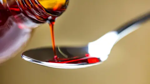 A close-up picture of red medicine being poured onto a silver spoon.