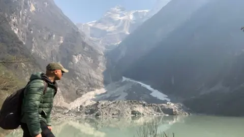 BBC World Service environment correspondent Navin Singh Khadka trekking with mountains visible behind him