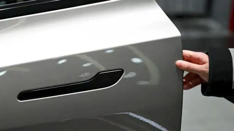 A customer inspects the minimalistic hidden door handles on an electric car in a showroom.
