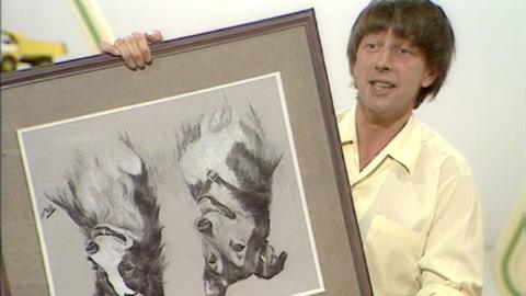 John Noakes holding a framed portrait of dogs Patch and Shep upside down.