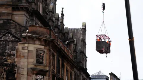 A burnt-out facade with men on a crane working on it