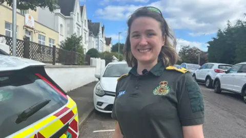 A young woman with brown hair wearing a green ambulance polo shirt