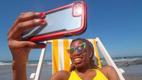 A woman takes a selfie in a deckchair on a beach