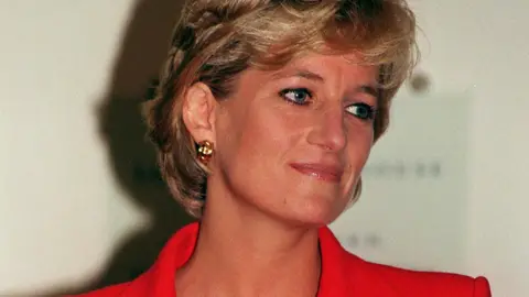 PA Media Princess Diana has short blonde hair and is wearing a bright red blazer. She is smiling and looking to the side.