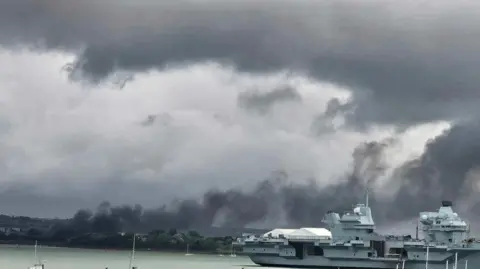 Katherine Floyd  A large cloud of smoke hovering over a marina