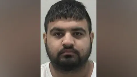 Mugshot of Hasan Mohammed. He has thick black hair and a thick black beard.
