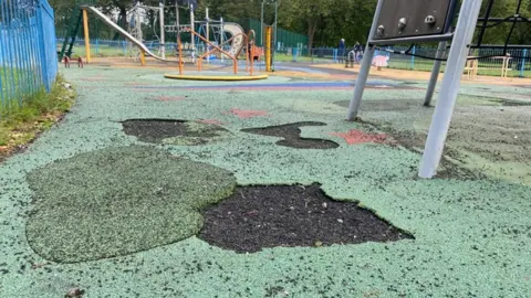 BBC Images show the soft rubber surface on a children's playground broken and missing in places around the bottom of some of the equipment