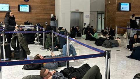 Groups of people sitting and lying on the floor between barriers at an airport