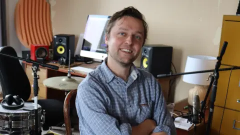 Joshua Burnside smiling in blue shirt with music equipment in the background