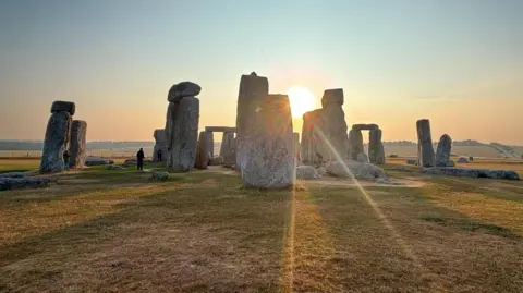 WeatherWatchers/Sukisnaps Light pour through a gap between stones at Stonehenge early in the morning.