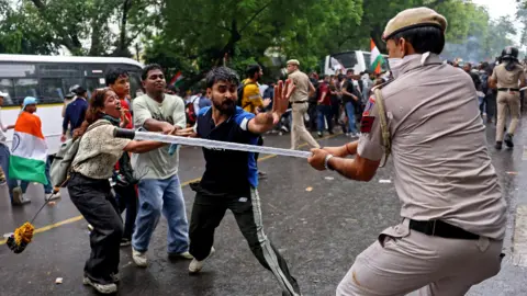 Reuters A security force personnel wields his baton against demonstrators following a clash during a planned march by supporters of India's Cockroach Janta Party towards parliament on the opening day of its monsoon session, demanding the resignation of Education Minister Dharmendra Pradhan over exam paper leaks, near Jantar Mantar, New Delhi