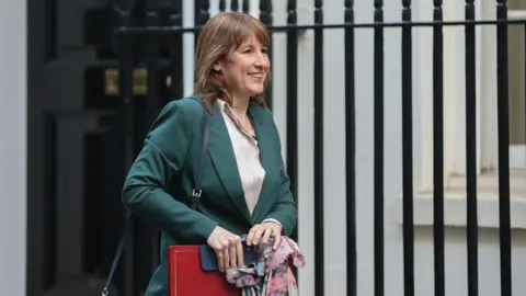 Rachel Reeves walking outside Number 11 Downing Street, smiling and wearing a green blazer.