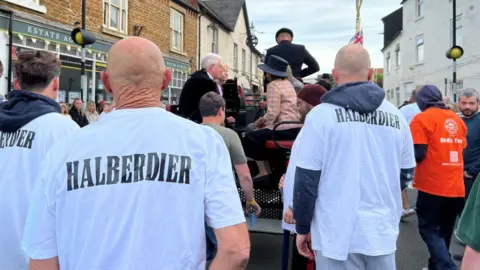 Carroll Weston/BBC Men in white T-shirts with the word "halberdier" printed on them in black. They stand around a carriage.