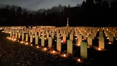 Stichting Adoptiegraven Foundation Stone graves in a war cemetery are lit up at night by candles 