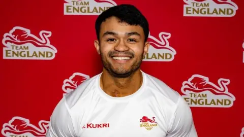 Jonathan Chin posing at a Team England media call. He is wearing a white Team England jersey.