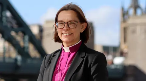 Diocese of Newcastle Bishop of Newcastle Helen-Ann Hartley wears a pink robe and brown glasses
