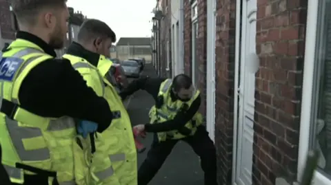 Police officers use a ram to break down a door