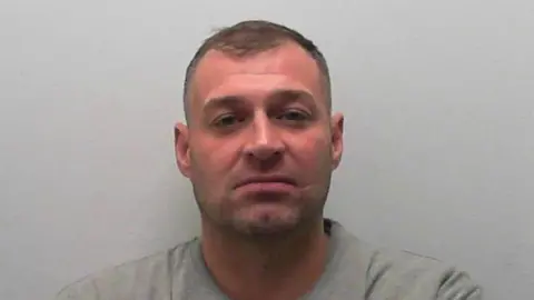A man in a grey prison tracksuit against a grey background