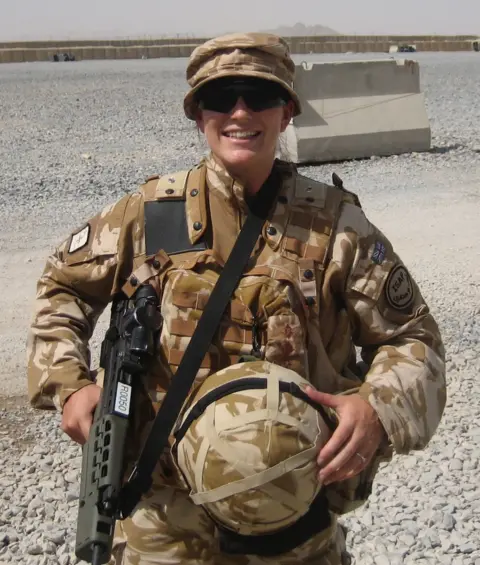 Bex Bennett Bex is wearing combat gear and holding a rifle and helmet