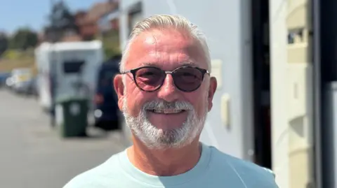 George King/BBC A head and shoulders shot of Ian Cable. He is smiling while looking directly into the camera. He is standing in front of his motorhome.