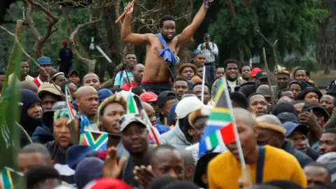 Anti-immigrant protesters with flags and sticks - one hoisted on the shoulders of other marchers in Durban, South Africa - 30 June 2026.