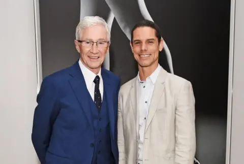 Getty Images Paul O'Grady in a blue suit and white shirt along with his husband André Portasio in a cream suit