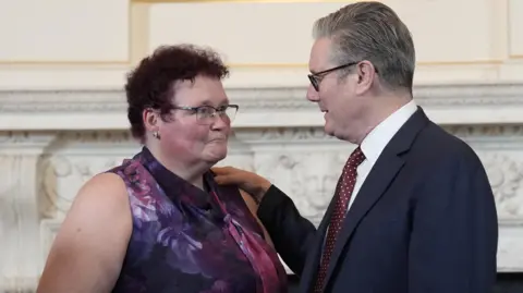 PA Media Prime Minister Sir Keir Starmer, wearing a dark suit and purple and white tie, with his hand on the shoulder of campaigner Claire Throssell, wearing a sleeveless purple top. 