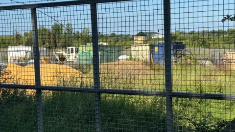 Photos of the site where allotments are meant to be built. Vehicles, building materials and piles of rubble could be seen from behind a fence.