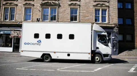 A white GeoAmey prison van driving past St Leonard's in Edinburgh. 