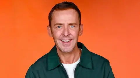 Radio presenter Scott Mills in a green shirt against an orange backdrop